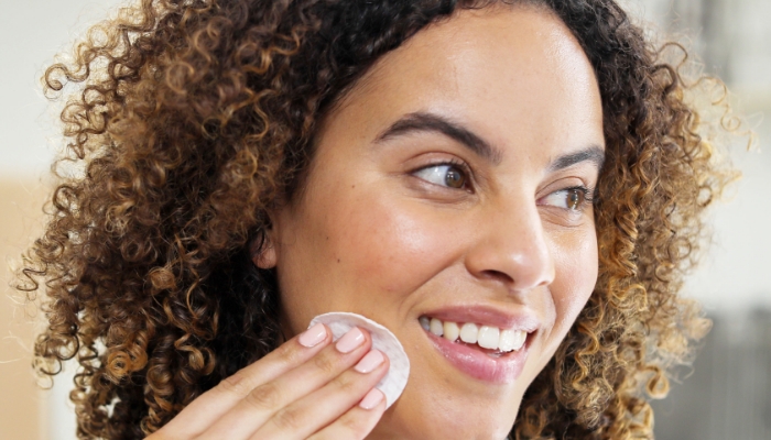 Image of a woman smiling and swiping Neora’s Acne Treatment Pads on her face